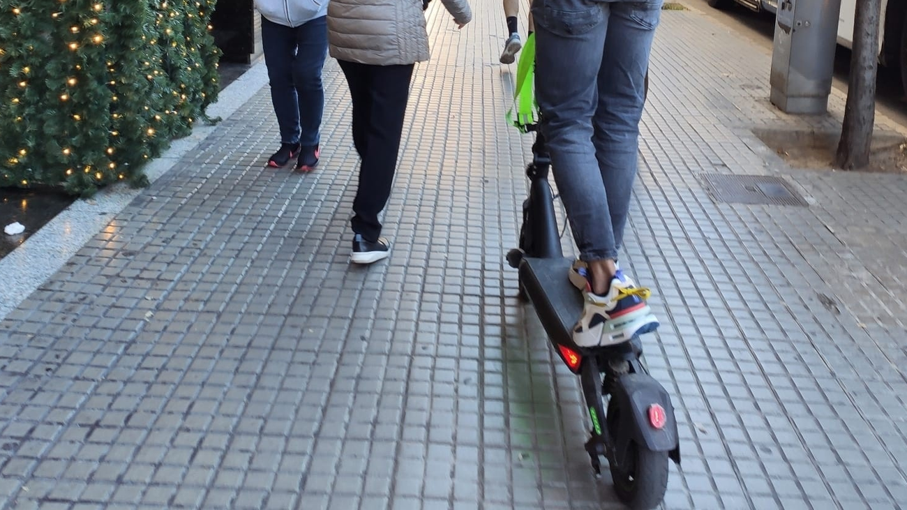 Una persona conduce un patinete por la acera entre peatones